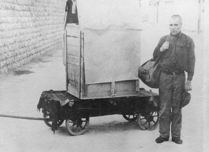 An escaped Mauthausen prisoner who has been apprehended by the SS is forced to pose next to the box in which he attempted his escape